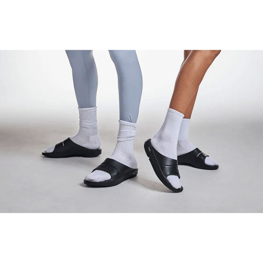 Two pairs of feet wearing black sandals and white socks on a light gray background