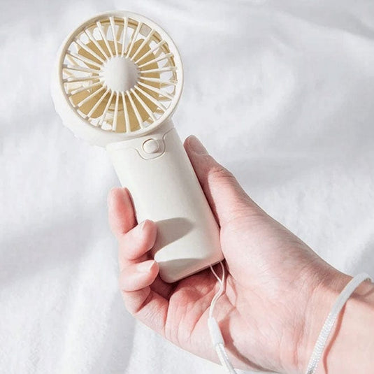 Hand holding a white handheld fan with gold accents on a light background
